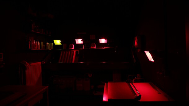 Dunkles Foto des Fotolabors. In rötlicher Färbung sind Arbeitsflächen und Lampen erahnbar